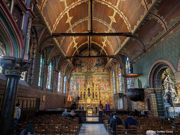 A partir da entrada, vimos o interior de uma igreja toda decorada de diferentes cores, com detalhes em madeira, pintura e itens esculpidos. O ambiente está bastante escuro.
